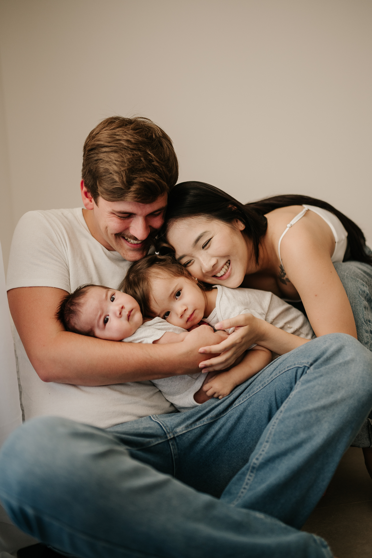 Pai e mãe sorrindo aconchegados no colo, segurando com carinho o bebê recém-nascido e a filha mais velha